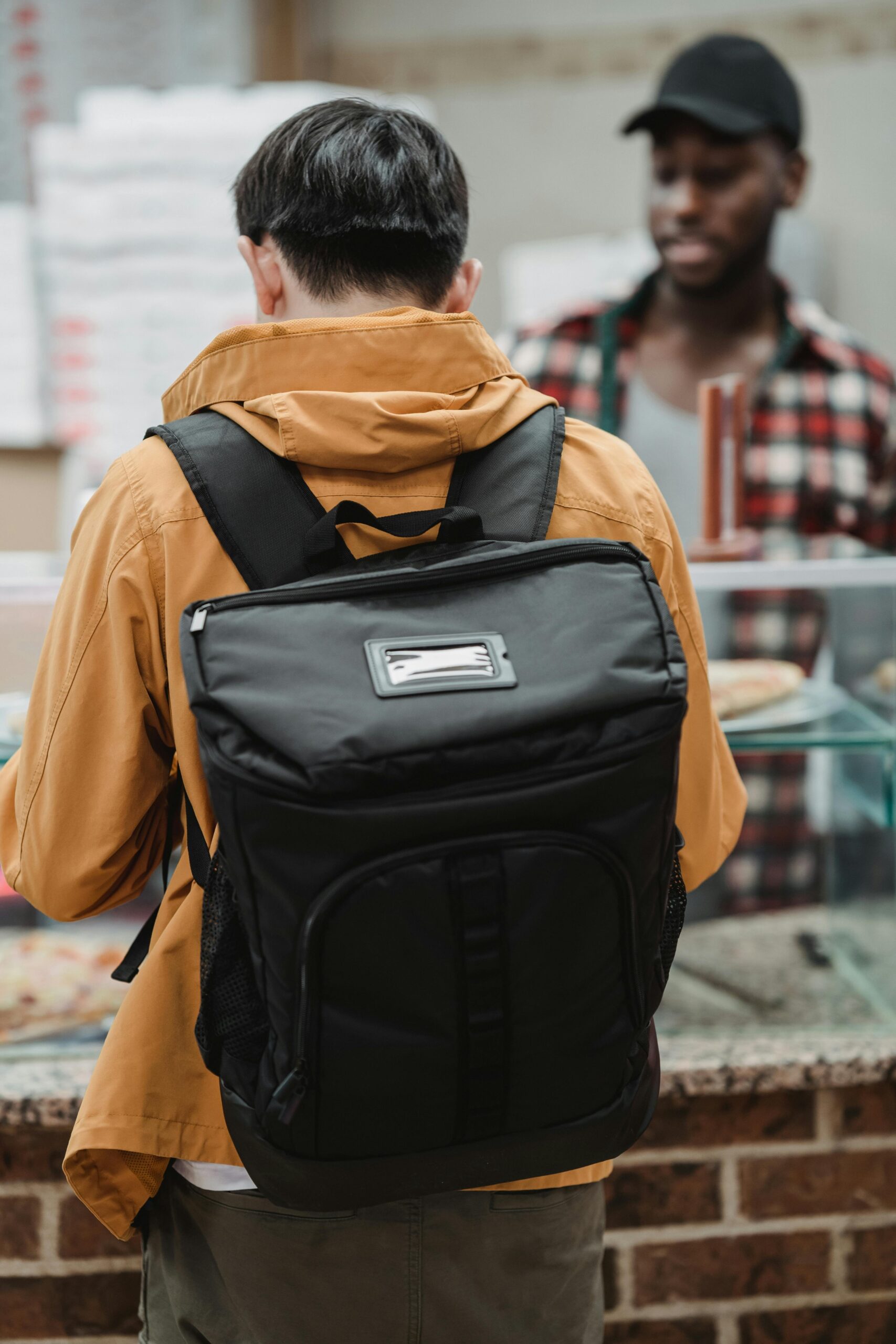 Person wearing a black travel backpack while standing at a food counter indoors